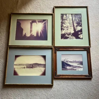 Sale Photo Thumbnail #104: Lot of four framed vintage photographs featuring a variety of scenic and travel subjects. Images include a dramatic sunburst through ancient classical ruins, a wooded forest scene, a snow-covered church or monastery in a mountainous landscape, and a panor