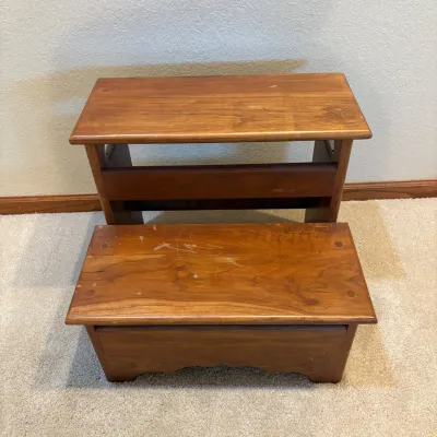 Sale Photo Thumbnail #184: This wooden step stool features a sturdy two-step design, perfect for reaching higher shelves or providing extra seating. Crafted from solid wood with a rich brown finish, it showcases natural wood grain patterns for an authentic rustic look. The stool me