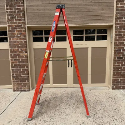 Sale Photo Thumbnail #206: This Werner step ladder features an 8-foot height, constructed with durable fiberglass for electrical safety and enhanced reliability. It has a bright orange color for high visibility on job sites and includes sturdy metal steps offering a secure footing.