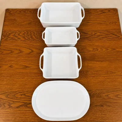 Sale Photo Thumbnail #132: This set features three high-quality Crate & Barrel baking dishes and a serving platter , crafted from durable white porcelain. Each dish is designed with convenient side handles for easy transport in and out of the oven. The dishes vary in size, with the