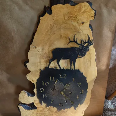 Rustic live-edge wood wall clock with a metal laser-engraved elk silhouette and a textured clock face with maple leaf detail