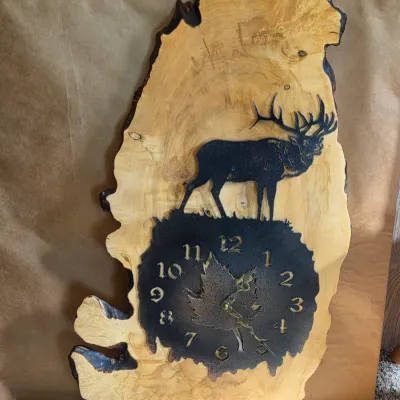 Rustic live-edge wood wall clock with a metal laser-engraved elk silhouette and a textured clock face with maple leaf detail