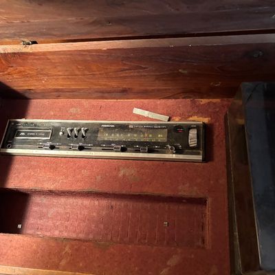 This vintage mid-century modern wooden stereo console features an integrated AM/FM radio and a top-loading record player turntable