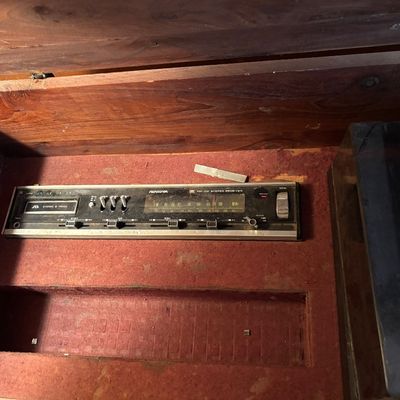 This vintage mid-century modern wooden stereo console features an integrated AM/FM radio and a top-loading record player turntable