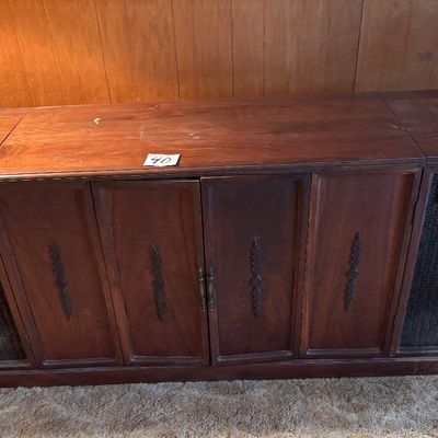 This vintage mid-century modern wooden stereo console features an integrated AM/FM radio and a top-loading record player turntable