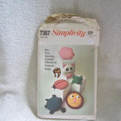 Sale Photo Thumbnail #6: Vintage Simplicity sewing pattern number 7367 for 'Cuddle Pillows or Pajama Bags'. This one-size pattern features several animal designs including a pig, cat, frog, ladybug, turtle, and lion. The paper envelope shows some wear, creasing, and tearing at th