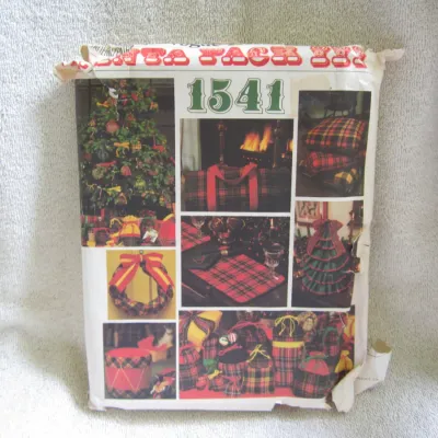 Sale Photo Thumbnail #32: Vintage Vogue sewing pattern number 1541, titled 'Santa Sack III'. Includes patterns for various Christmas and holiday home decor crafts such as a wreath, placemats, decorative tree, gift bags, cushions, and a duffel bag, primarily styled in plaid. The pa