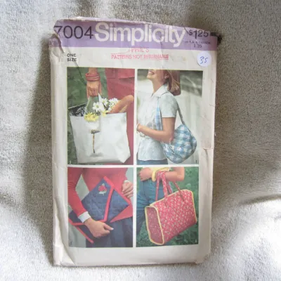Sale Photo Thumbnail #36: Vintage Simplicity sewing pattern number 7004 for one-size bags and totes. Includes patterns for a tote bag, shoulder bag, quilted clutch, and quilted tote. The envelope shows vintage wear, including creasing, minor tears along the top edge, a retail stam
