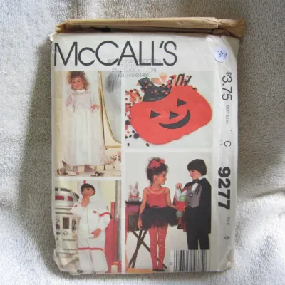 Sale Photo Thumbnail #40: Vintage McCall's sewing pattern number 9277 for children's costumes, size 6. Features designs for a pumpkin, astronaut, magician, bride, and devil/fairy. The envelope shows wear, creasing, and minor tearing at the top flap. Pattern pieces and instructions