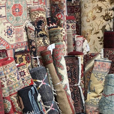 Extensive assortment of rolled handmade rugs featuring traditional medallions, florals, geometric designs, and richly detailed borders.