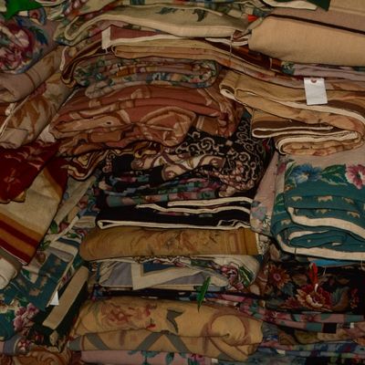 Stacked assortment of colorful folded rugs showcasing a variety of woven patterns, textures, and traditional designs available throughout...