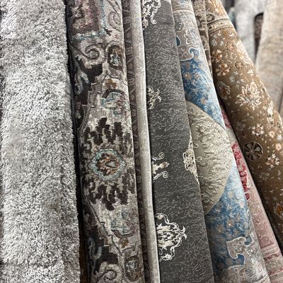 Close-up collection of rolled rugs featuring black, ivory, blue, and neutral designs with intricate traditional floral patterns.