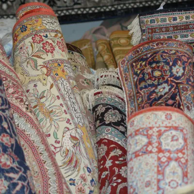 Collection of rolled traditional rugs showcasing rich floral patterns and intricate designs in red, blue, ivory, gold, and pastel tones.