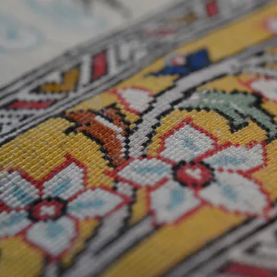 Close-up showcasing a colorful geometric handwoven design with blue, yellow, ivory, pink, and muted green detailing.
