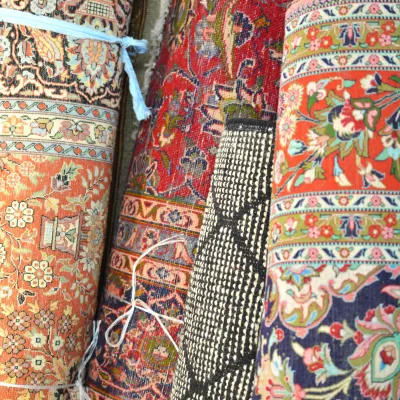 Colorful assortment of rolled handmade rugs showcasing intricate floral, geometric, and traditional designs in vibrant warm tones.