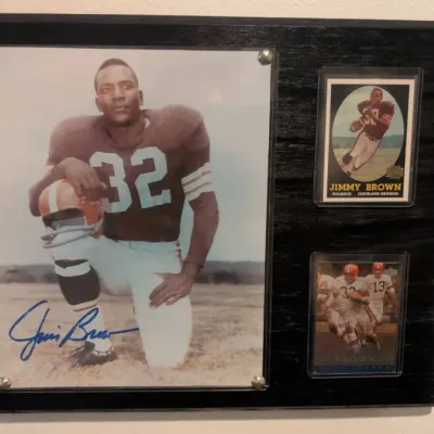 Hand-signed Jim Brown 8x10 photograph alongside two vintage Cleveland Browns football cards