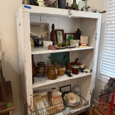 Chippy white primitive cupboard with antique bottles and stoneware
