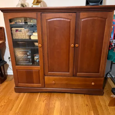 Sale Photo Thumbnail #39: Traditional cherry-finished wooden entertainment center featuring a glass-front display cabinet on the left, double arched-panel doors, and a wide bottom drawer.