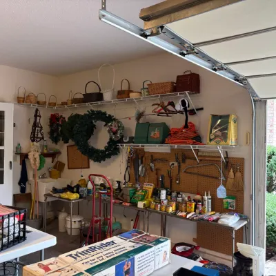 Sale Photo Thumbnail #9: Assorted garage and household items, including a collection of woven baskets, holiday wreaths, hand tools on a pegboard, and a vintage TrimRider exercise machine in its original box.