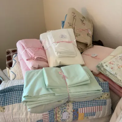 Sale Photo Thumbnail #37: Assorted vintage bed linens and quilts, including a mint green sheet set and a blue-and-white patchwork quilt, neatly bundled and tagged for sale.