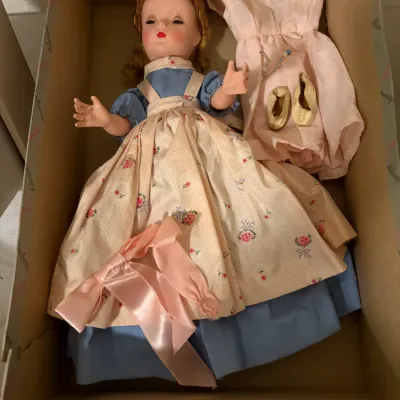 Sale Photo Thumbnail #84: Vintage Madame Alexander doll in a blue dress and floral pinafore, complete with an extra pink dress, gold shoes, and accessories in its original box.