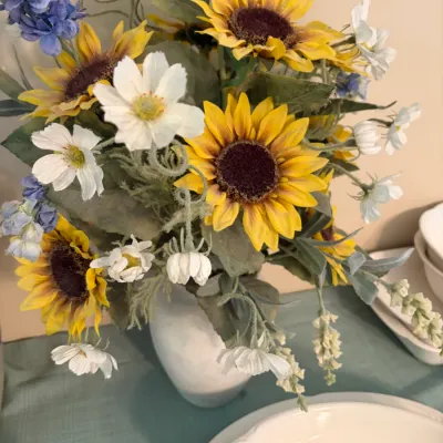 Sale Photo Thumbnail #61: Artificial floral arrangement featuring sunflowers, white daisies, and blue accent flowers in a simple white ceramic vase.