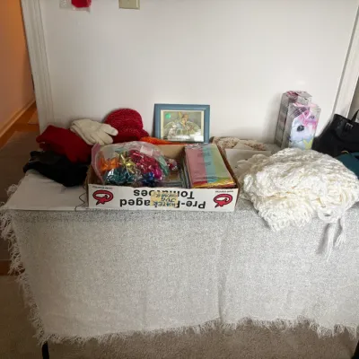 Sale Photo Thumbnail #23: Tabletop display featuring a variety of items including winter accessories, gift wrapping supplies, a white crocheted shawl, and handbags.