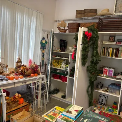 Sale Photo Thumbnail #2: An assortment of holiday decorations, books, board games, and household items displayed on shelves and tables.