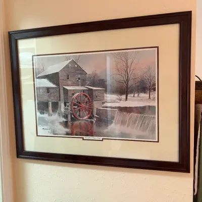 Sale Photo Thumbnail #93: Framed art print titled "Snowfall in Pigeon Forge" by Michael Sloan, depicting a rustic winter grist mill scene with a prominent red water wheel. The piece is double-matted and housed in a dark wood frame.