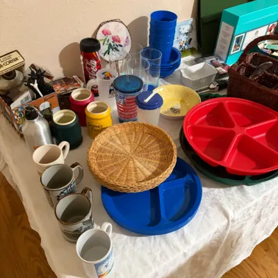 Sale Photo Thumbnail #55: Assorted collection of vintage and modern kitchenware, featuring ceramic mugs, colorful plastic divided plates, wicker plate holders, and various tumblers.