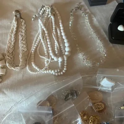 Sale Photo Thumbnail #122: Assortment of vintage costume jewelry, including white beaded necklaces, a faceted crystal necklace, and various clip-on earrings in individual plastic bags.