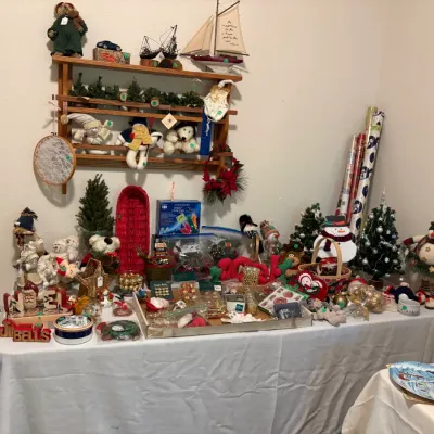 Sale Photo Thumbnail #30: Assortment of festive Christmas decorations, featuring snowman figurines, plush holiday characters, miniature trees, wrapping paper, and a wooden wall shelf displaying a model sailboat.