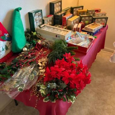 Sale Photo Thumbnail #42: Collection of vintage Christmas decorations, including boxed glass ornaments, faux poinsettias, holly sprigs, and a green felt elf hat arranged on a table.