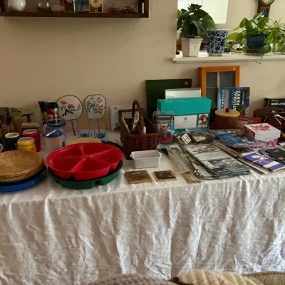 Sale Photo Thumbnail #16: Assorted household items, kitchenware, and office supplies displayed on a table, including mugs, woven plate holders, a red divided serving tray, and stationery.