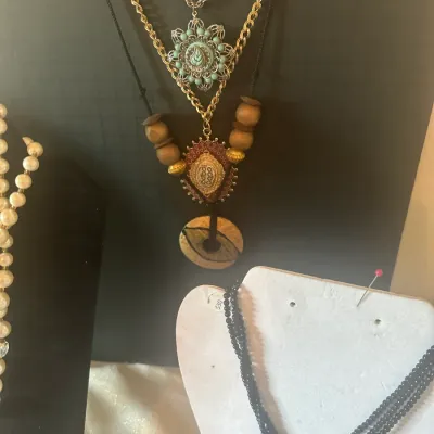 Sale Photo Thumbnail #121: Selection of vintage costume jewelry necklaces, including a bohemian-style layered display with wooden beads and filigree pendants, alongside a multi-strand black beaded necklace.