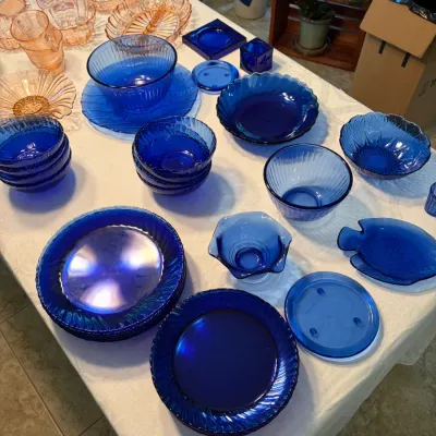 Sale Photo Thumbnail #56: Collection of vintage cobalt blue glassware, including plates, bowls, and a fish-shaped dish, displayed alongside pink depression glass pieces.