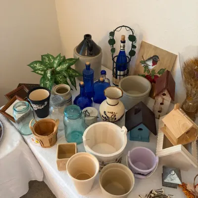 Sale Photo Thumbnail #91: An assortment of rustic farmhouse decor, featuring cobalt blue glass bottles, stoneware crocks and jugs, wooden birdhouses, and vintage mason jars.