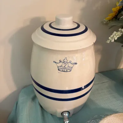 Sale Photo Thumbnail #62: Vintage Robinson Ransbottom 2-gallon stoneware water cooler crock with a matching lid, featuring blue stripes, a blue crown logo, and a metal spigot.