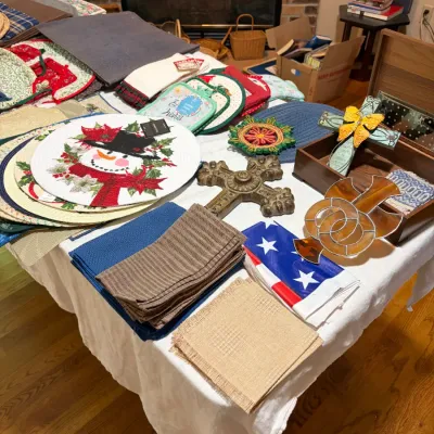 Sale Photo Thumbnail #46: Assortment of home decor and kitchen linens, featuring holiday-themed placemats, cloth napkins, potholders, and decorative crosses.