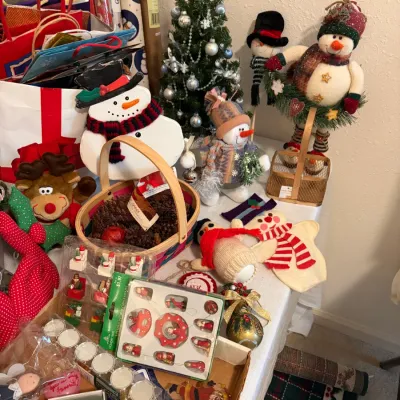 Sale Photo Thumbnail #79: Assortment of festive Christmas decorations, featuring various snowman figurines, a small decorated artificial tree, miniature wooden ornaments in original packaging, and a basket of pinecones.