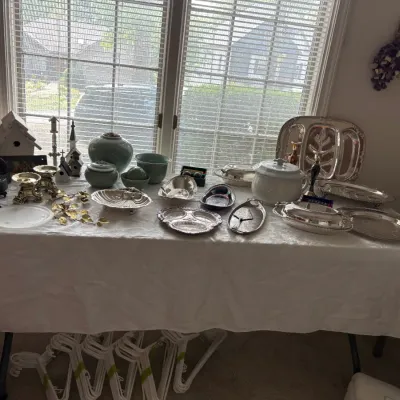 Sale Photo Thumbnail #25: Assorted vintage silver-plated serving ware, including platters, bowls, and a tureen, displayed alongside celadon green ceramic pottery, brass candlesticks, and decorative home accents.
