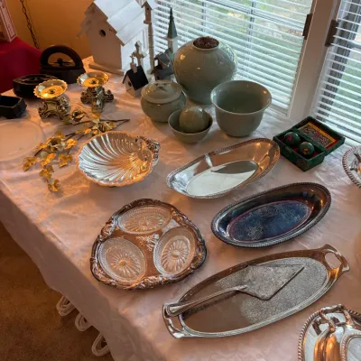Sale Photo Thumbnail #41: An assortment of vintage home decor featuring silver-plated serving platters, a shell-shaped dish, celadon green ceramic pottery, and brass candlesticks.