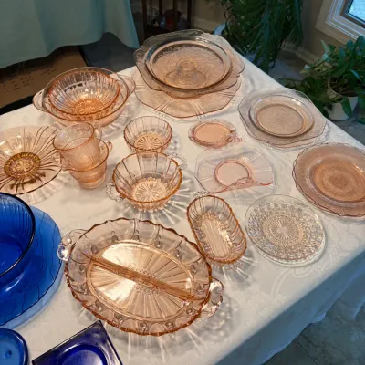 Sale Photo Thumbnail #58: Assortment of vintage pink depression glass tableware, including plates, bowls, cups, and a divided serving dish, displayed alongside select cobalt blue glassware.