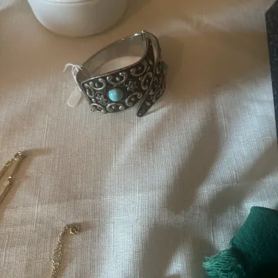 Sale Photo Thumbnail #120: Ornate silver-toned cuff bracelet featuring intricate scrollwork, floral motifs, and a turquoise cabochon stone, displayed alongside other vintage jewelry pieces.