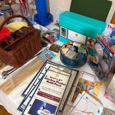 Sale Photo Thumbnail #54: Assorted household items and stationery, featuring a woven wicker utensil basket, a Burgoyne handmade greeting card box, photo album refill pages, and a tin filled with vintage matchboxes.