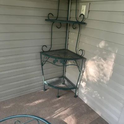 Sale Photo Thumbnail #108: Green wrought iron corner bakers rack featuring four mesh shelves, decorative scrollwork, and leaf accents, suitable for indoor or outdoor patio use.