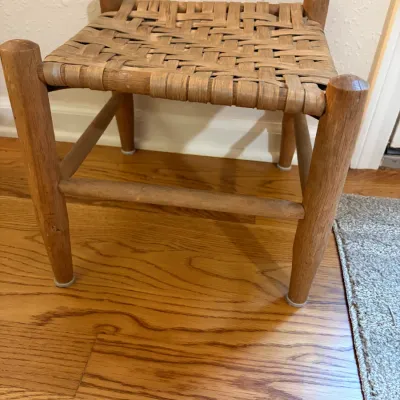 Sale Photo Thumbnail #50: Vintage rustic wooden footstool featuring a woven splint seat and sturdy round legs with stretchers, showing light wear consistent with age.