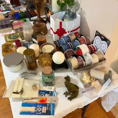 Sale Photo Thumbnail #51: Assorted craft supplies and home decor items, featuring rolls of decorative ribbon, various pillar and jar candles, oil lamp wicks, and a ceramic frog figurine.