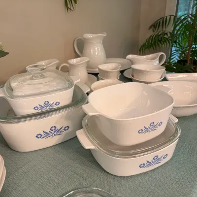 Sale Photo Thumbnail #85: Vintage CorningWare 'Blue Cornflower' casserole dishes with glass lids, displayed alongside coordinating white ceramic tableware including pitchers and bowls.
