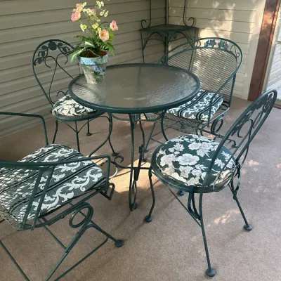 Sale Photo Thumbnail #107: Vintage green metal patio dining set including a round glass-top table, four chairs with decorative scrollwork and patterned cushions, and a matching corner baker's rack.